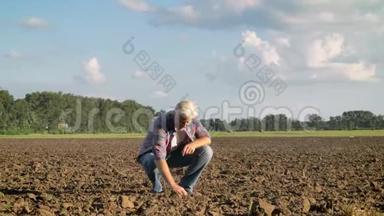 在炎热的夏日里，老农坐在田里，一手抓土